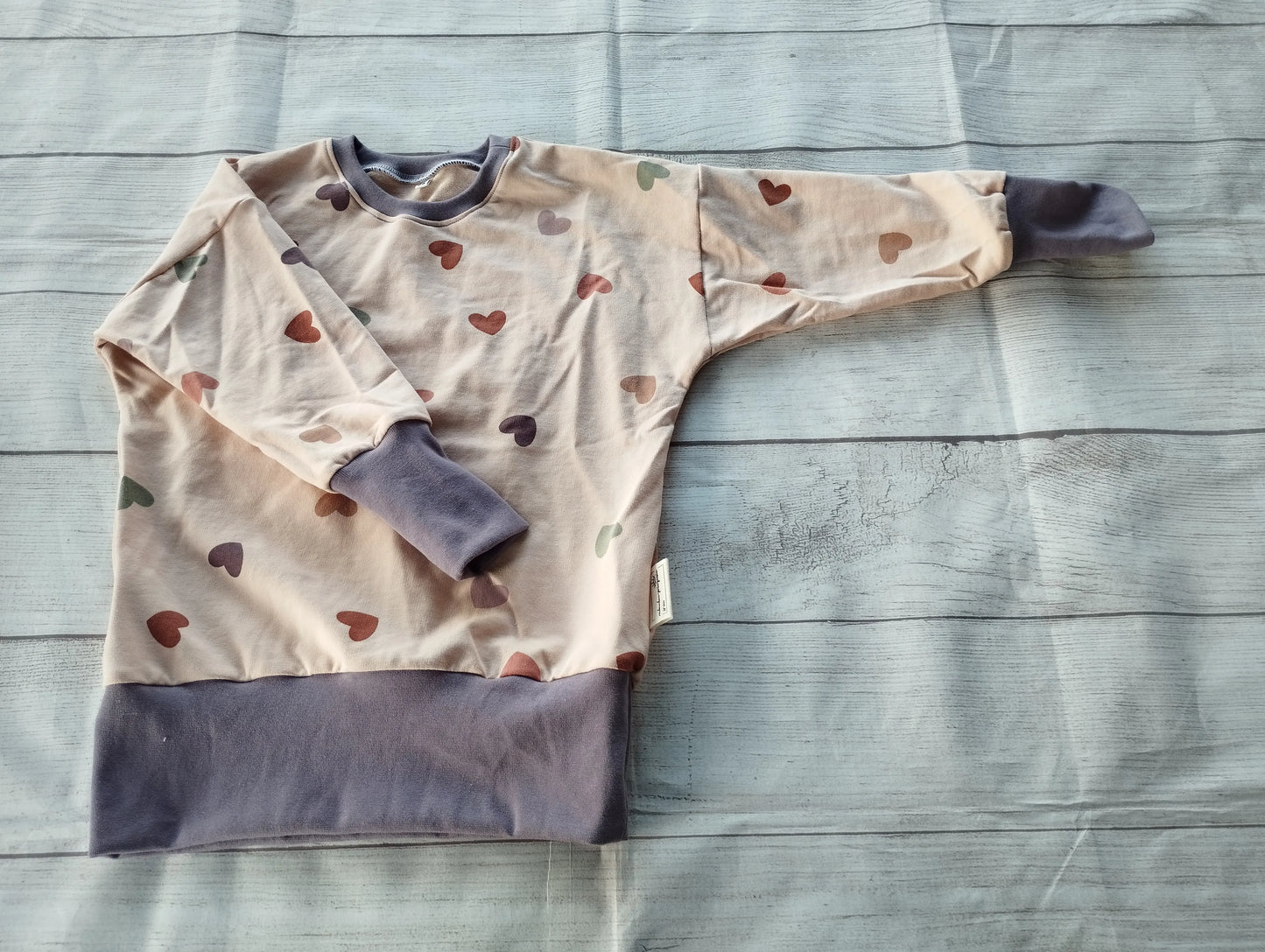 Kinderpullover mit Herzchen-Muster aus OEKO-TEX zertifiziertem French Terry, handgemacht in Oldenburg, Einzelgröße, beige mit lilafarbenen Bündchen.