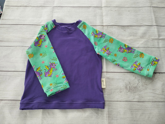 Kinder-Raglanshirt mit unifarbenem lila Vorderteil und grünen Ärmeln mit Drachen-Muster – handgemacht aus elastischem Baumwolljersey