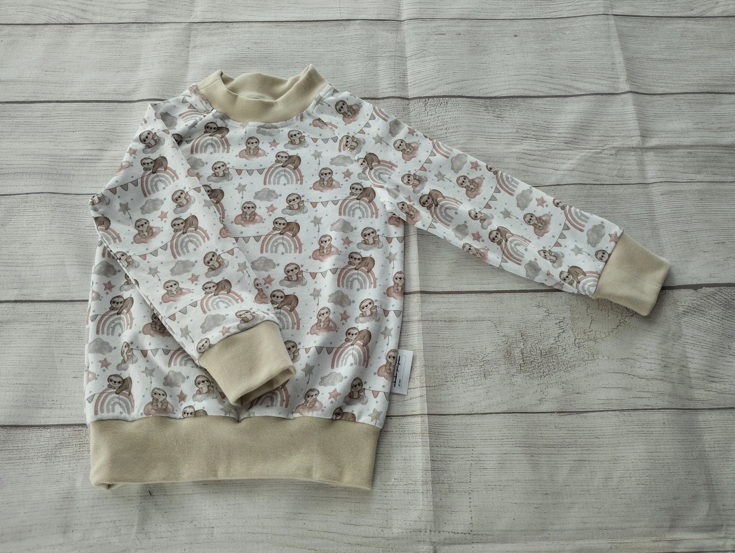 Kinder-Raglanshirt mit Faultier- und Regenbogen-Muster in Pastellfarben und beigefarbenen Bündchen – handgemacht aus elastischem Baumwolljersey