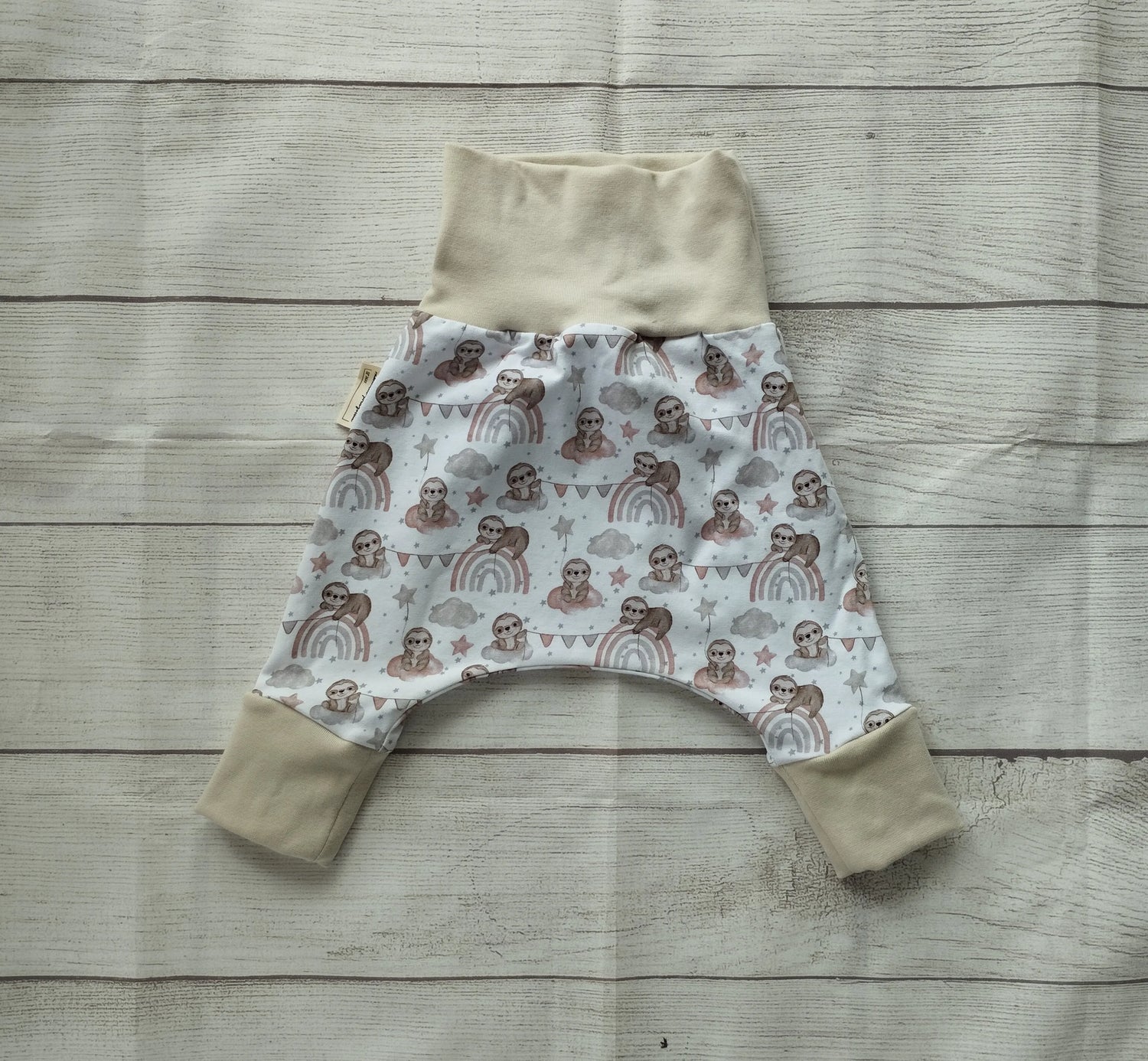 Mitwachshose für Babys mit Faultier- und Regenbogen-Muster auf pastellfarbenem Stoff und beigefarbenen Bündchen – handgemacht aus elastischem Baumwolljersey