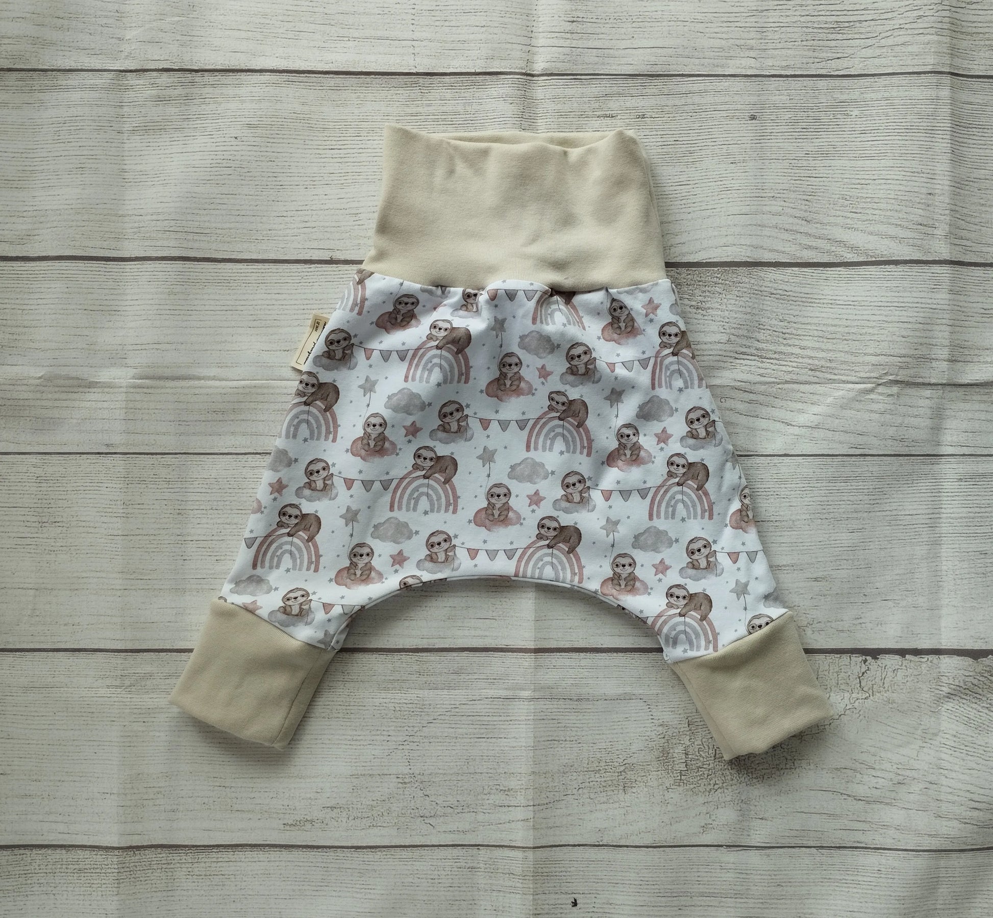Mitwachshose für Babys mit Faultier- und Regenbogen-Muster auf pastellfarbenem Stoff und beigefarbenen Bündchen – handgemacht aus elastischem Baumwolljersey