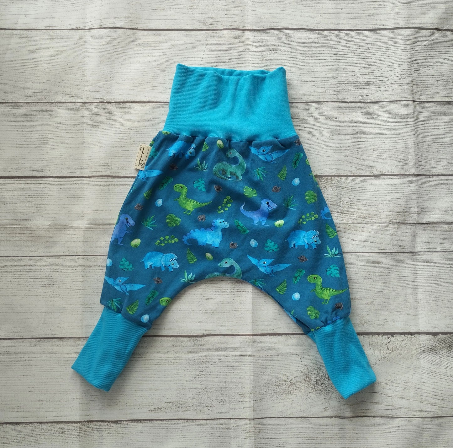 Mitwachshose für Babys mit buntem Dinosaurier-Muster auf blauem Stoff und türkisfarbenen Bündchen – handgemacht aus elastischem Baumwolljersey