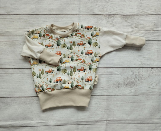 Mitwachspullover für Babys mit buntem Fahrzeug-Design, flach auf Holzoberfläche präsentiert