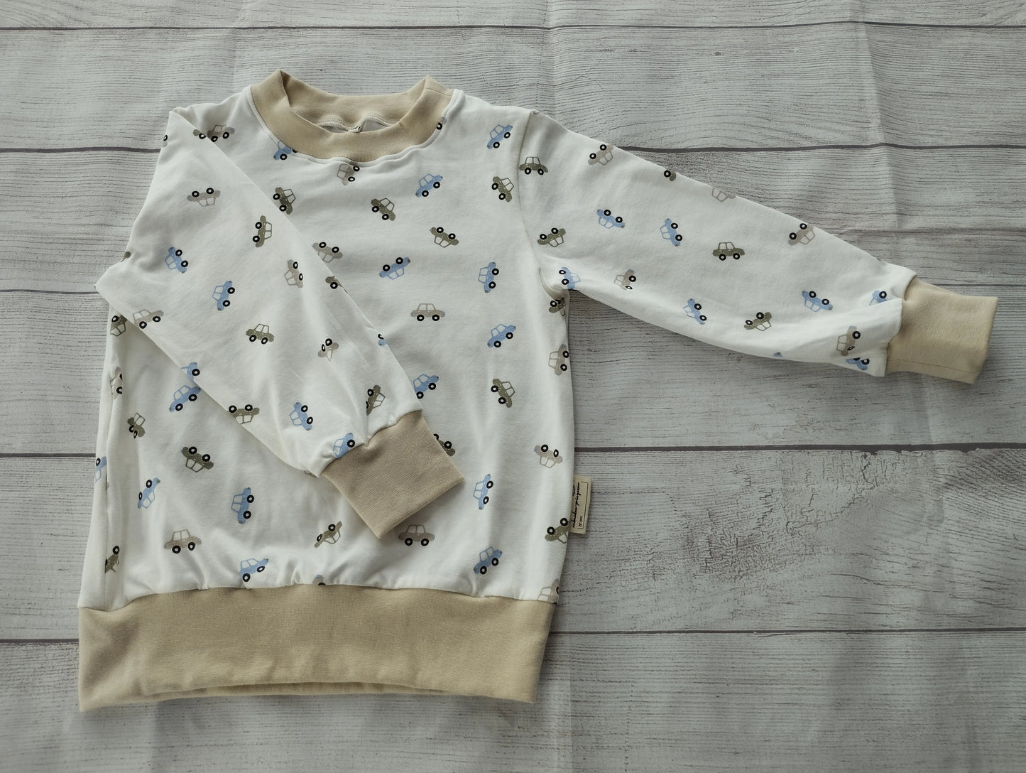 Kinderpullover mit buntem Auto-Muster auf weißem Stoff und beigefarbenen Bündchen – handgemacht aus elastischem Baumwolljersey