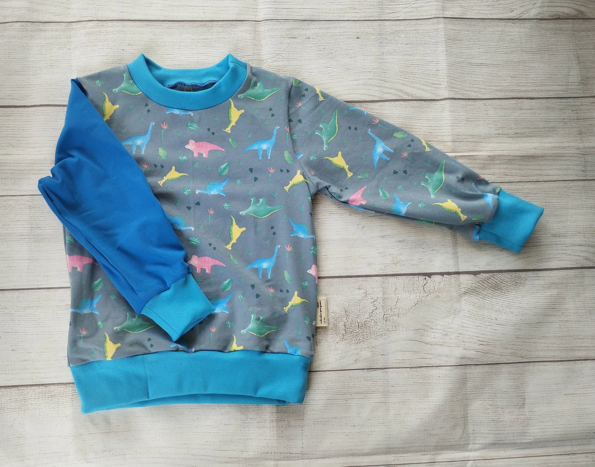 Kinderpullover mit buntem Dino-Muster und blauem Ärmel – handgemacht aus elastischem Baumwolljersey