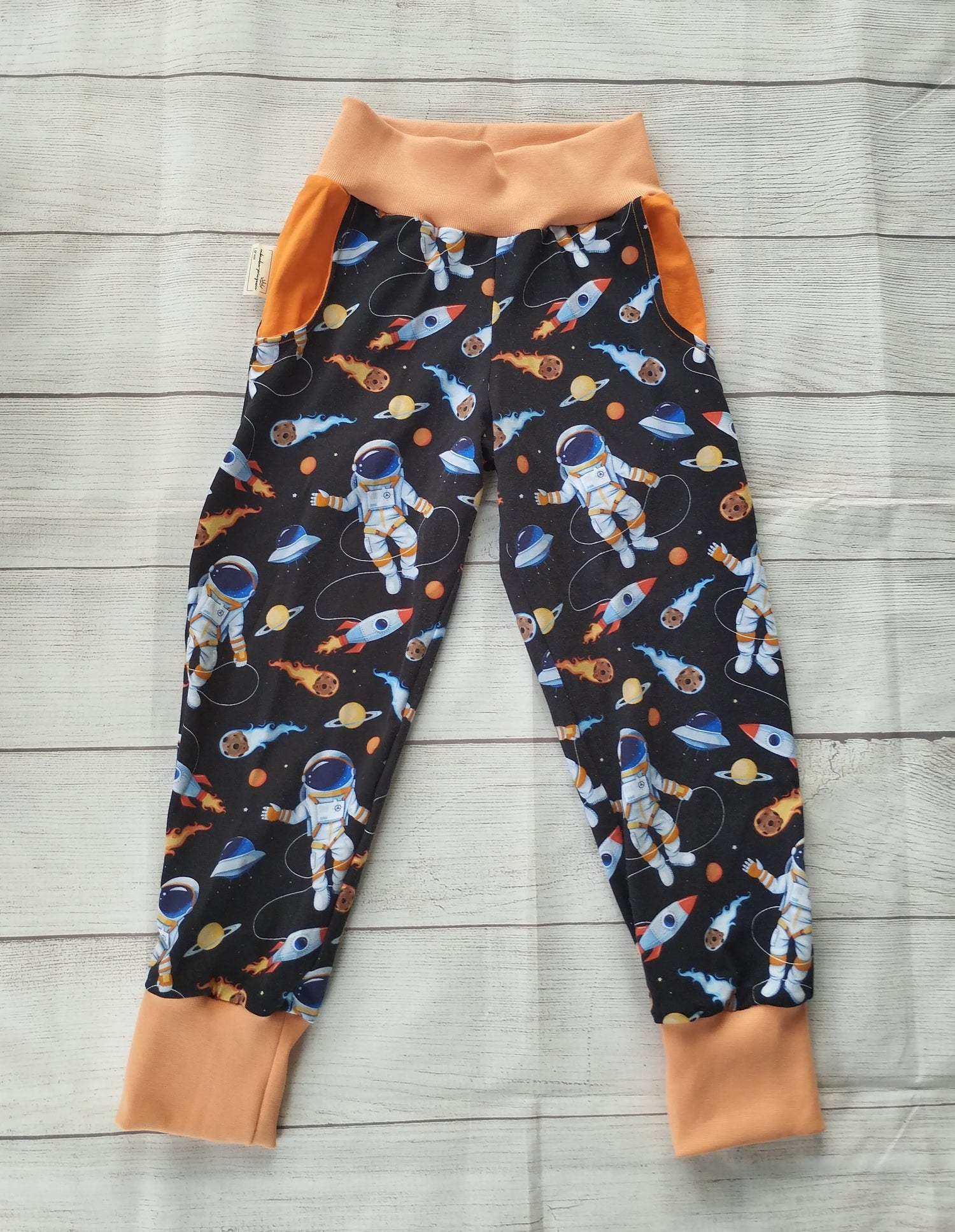 Kinder-Pumphose mit Astronauten-, Raketen- und Planeten-Muster auf dunklem Stoff mit orangefarbenen Bündchen – handgemacht aus elastischem Baumwolljersey