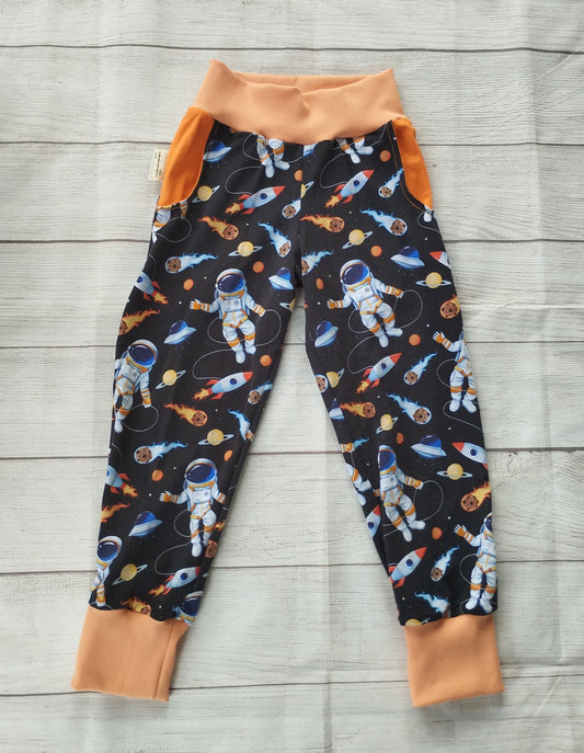 Kinder-Pumphose mit Astronauten-, Raketen- und Planeten-Muster auf dunklem Stoff mit orangefarbenen Bündchen – handgemacht aus elastischem Baumwolljersey