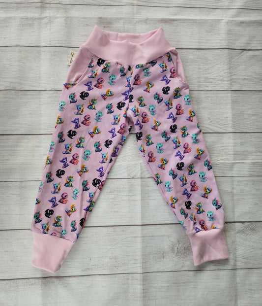Handgemachte Pumphose mit buntem Drachenmotiv auf rosa Grund, flach ausgelegt auf hellem Holz – elastischer Baumwolljersey mit rosa Bündchen.
